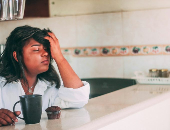 Mujer con dolor de cabeza junto a un café, posible síntoma del déficit de DAO