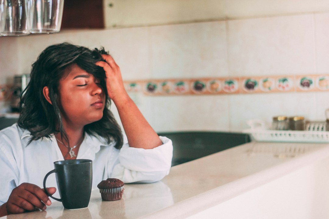 Mujer con dolor de cabeza junto a un café, posible síntoma del déficit de DAO